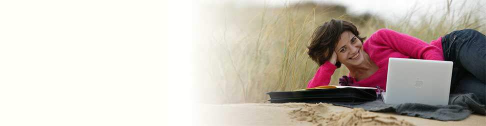 Woman using computer on the dunes near a beach.